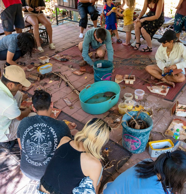 people sitting in a circle concentrating on a painting on bark